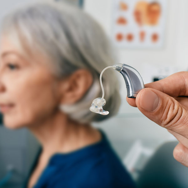 closeup of a modern hearing aid with senior woman in the background